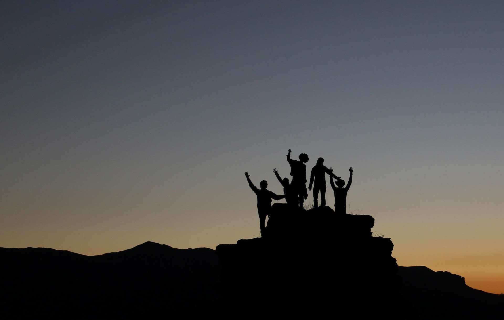 Silhouette of people on top of a mountain peak cheering during sunset. Photo by Natalie Pedigo on Unsplash