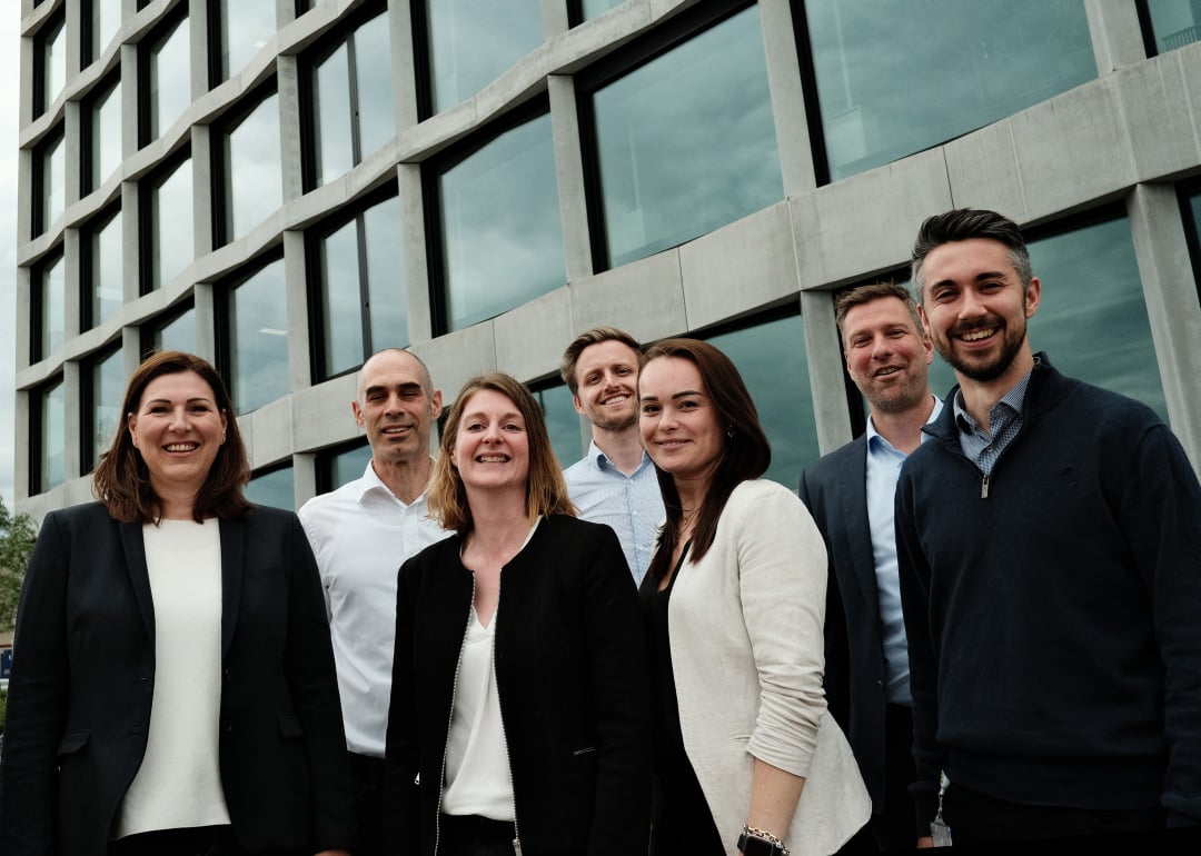 Seven people, men and women smiling in front of a office building