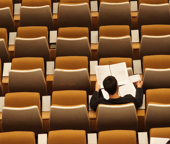 Single student sitting in a lecture hall surrounded by empty seats